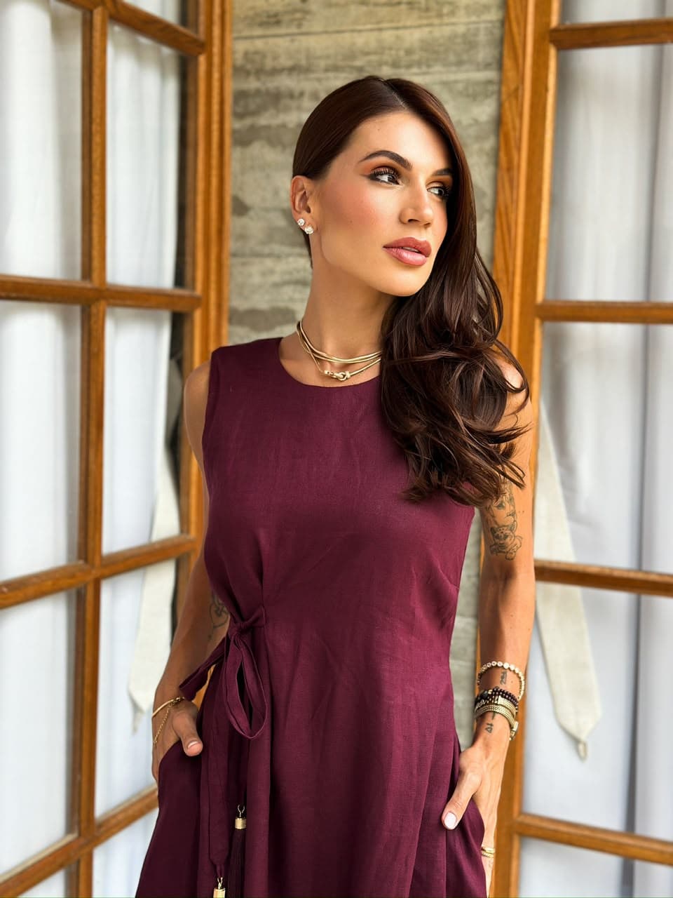Juliana Santos com vestido vinho junto à janela